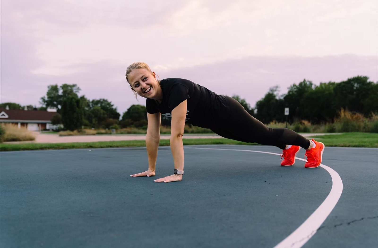 Bri holding a plank on an outdoor court at dusk